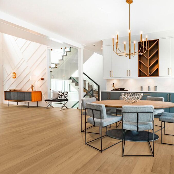 Unser Premium-Laminat Raumfoto eines Laminats in hellbrauner Holzoptik in einem offenen Wohnbereich in den Farben Grau, Hellbraun und Gold. Im Hintergrund ist ein runder Esszimmertisch sichtbar.